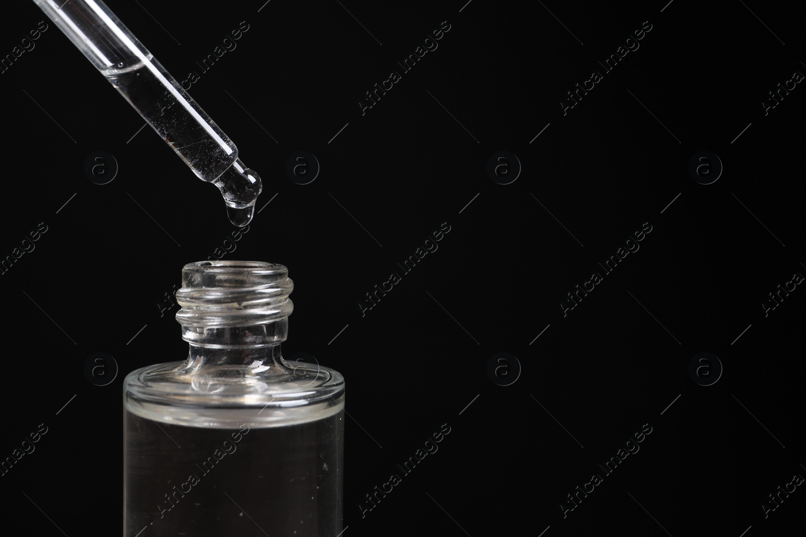 Photo of Dripping cosmetic serum from pipette into bottle on black background, closeup. Space for text