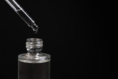 Photo of Dripping cosmetic serum from pipette into bottle on black background, closeup. Space for text