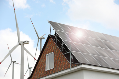 Wind turbines near house with installed solar panels on roof. Alternative energy source