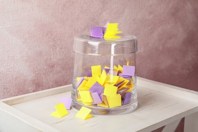 Photo of Colorful paper pieces for lottery and glass container on wooden table