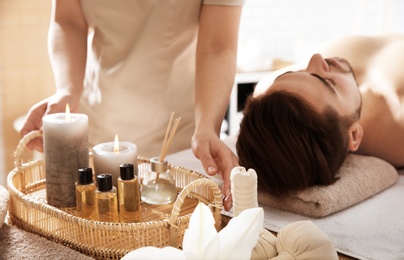 Massage therapist with spa essentials and young man in wellness center