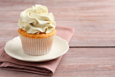 Photo of Tasty cupcake with vanilla cream on pink wooden table, closeup. Space for text