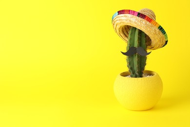 Photo of Cactus with Mexican sombrero hat and fake mustache on yellow background, space for text