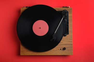 Photo of Modern vinyl record player with disc on red background, top view