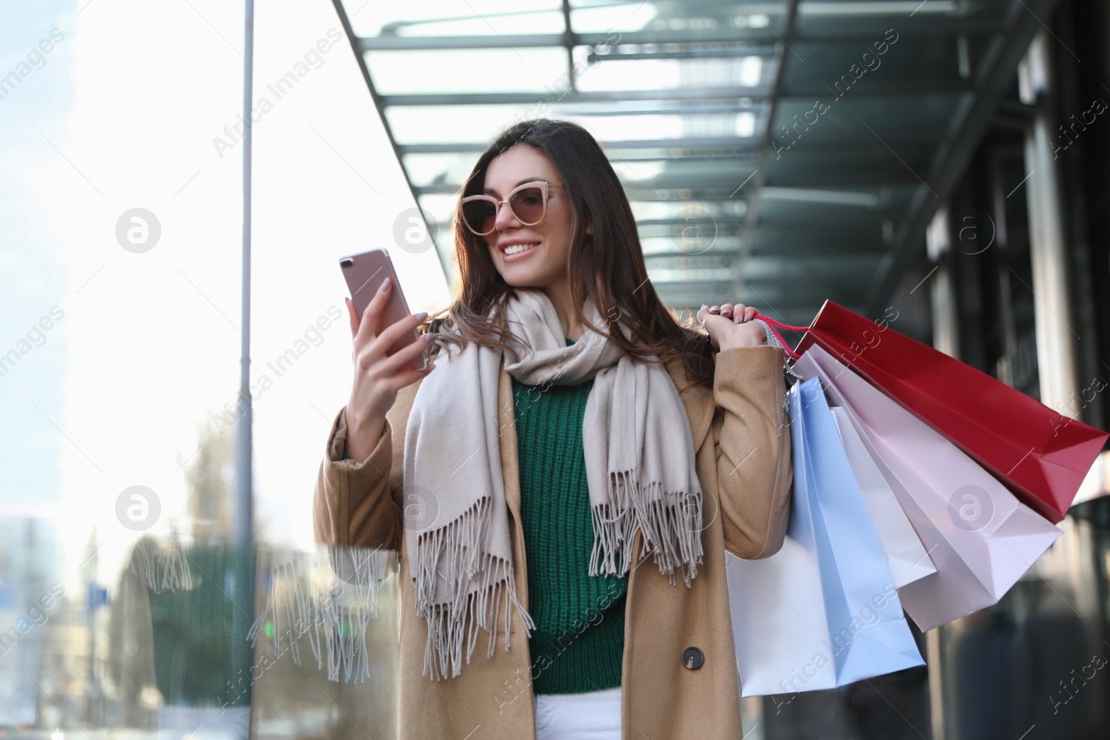 Photo of Beautiful young woman with shopping bags and smartphone outdoors