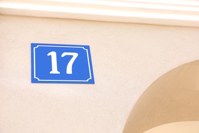 Photo of Plate with house number seventeen on beige wall outdoors. Space for text