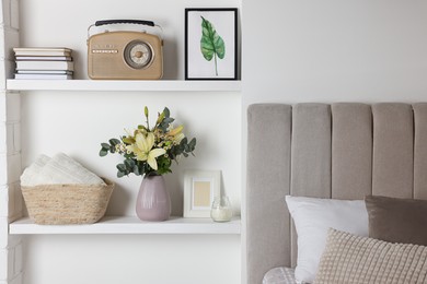 Photo of Stylish vase with flowers, retro radio and decor on shelves indoors. Bedroom interior elements