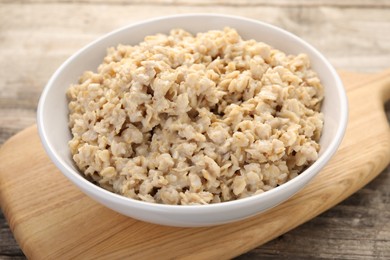 Photo of Tasty boiled oatmeal in bowl on wooden table, closeup