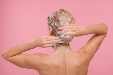 Woman washing hair on pink background, back view