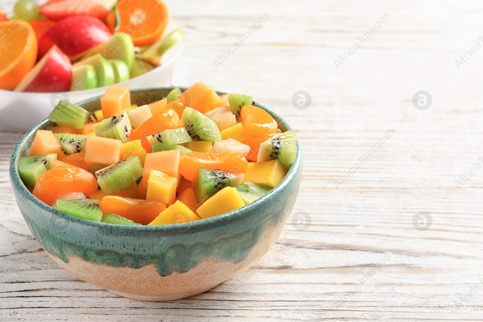 Photo of Bowl with fresh cut fruits on wooden table