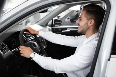 Young man testing new car in salon