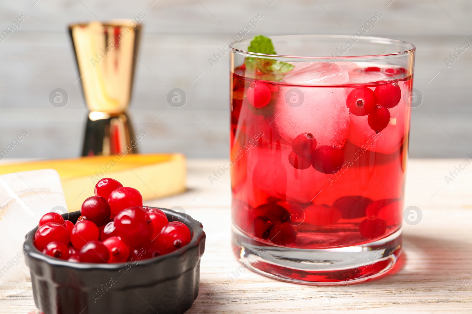 Photo of Tasty cranberry cocktail with ice cubes in glass and fresh berries on wooden table