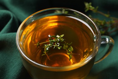 Photo of Glass cup of aromatic herbal tea with thyme on green fabric, closeup