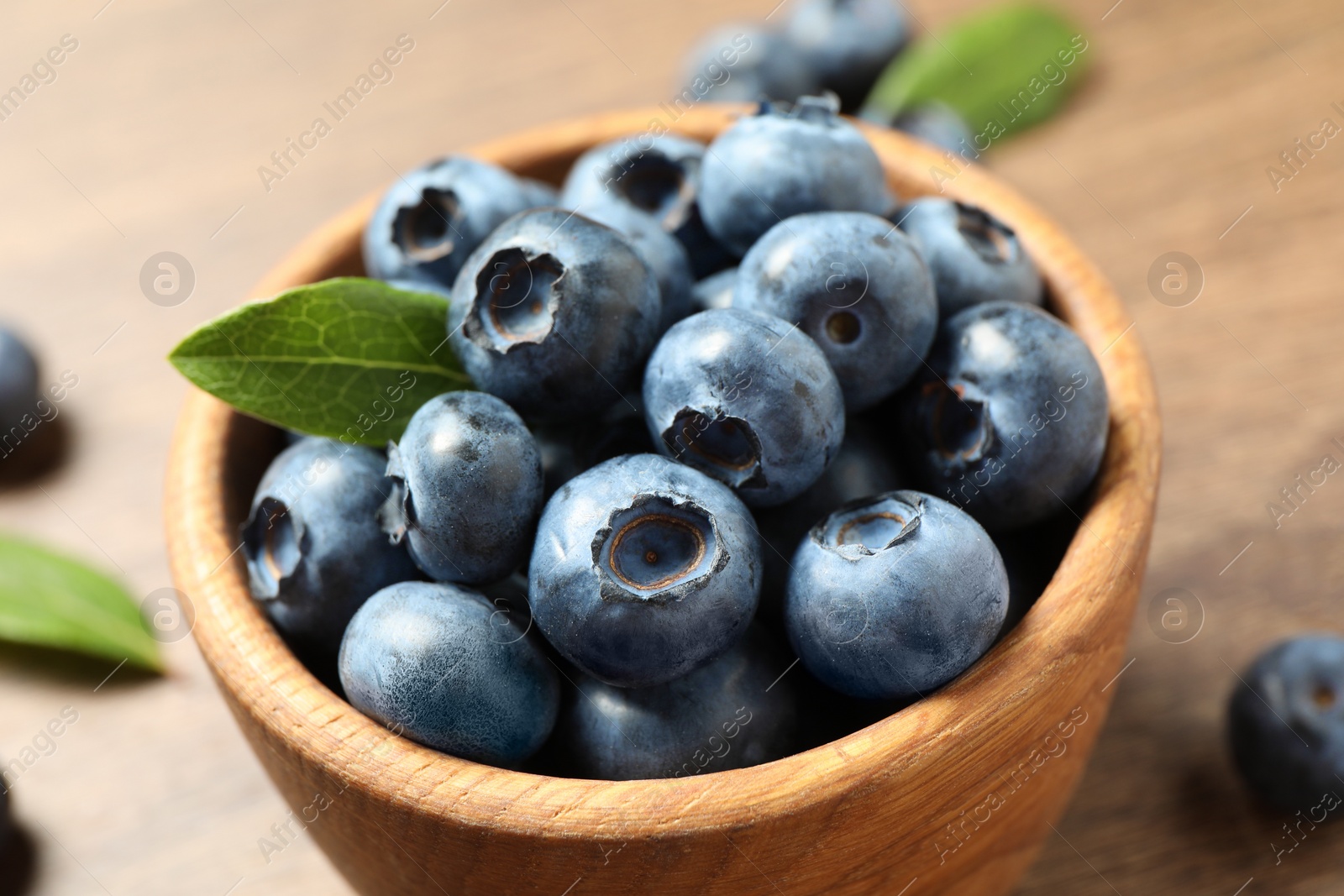 Photo of Bowl of tasty fresh blueberries with green leaves on table, closeup