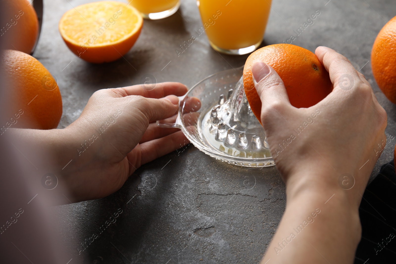 Photo of Woman squeezing orange juice at grey table, closeup