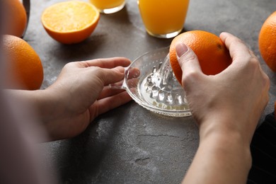 Woman squeezing orange juice at grey table, closeup