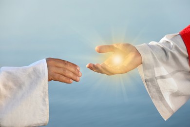 Image of Jesus Christ and man near water outdoors, closeup. Miraculous light in hand
