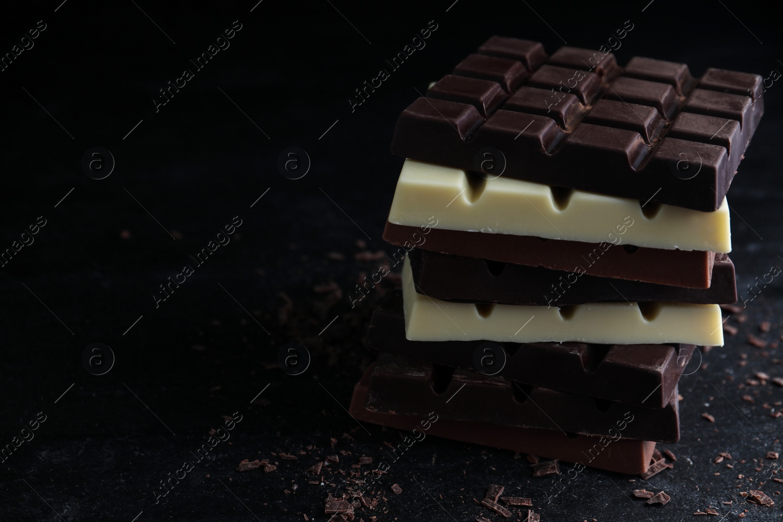 Photo of Different tasty chocolate bars on black table. Space for text