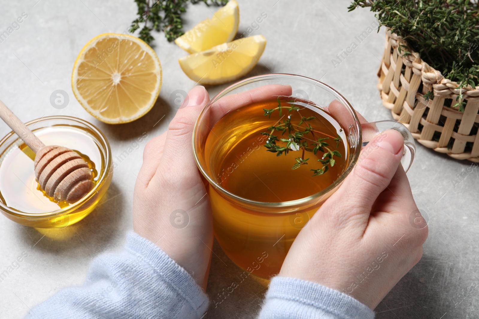 Photo of Woman holding cup of tasty herbal tea with thyme at light grey table, closeup