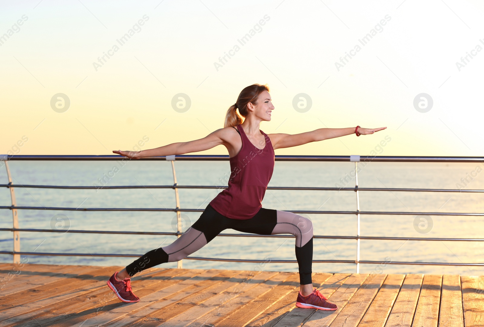 Photo of Young woman doing fitness exercises on pier in morning