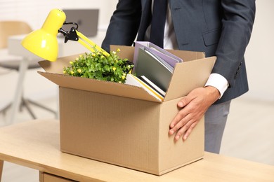Photo of Unemployment problem. Man with box of personal belongings at table in office, closeup