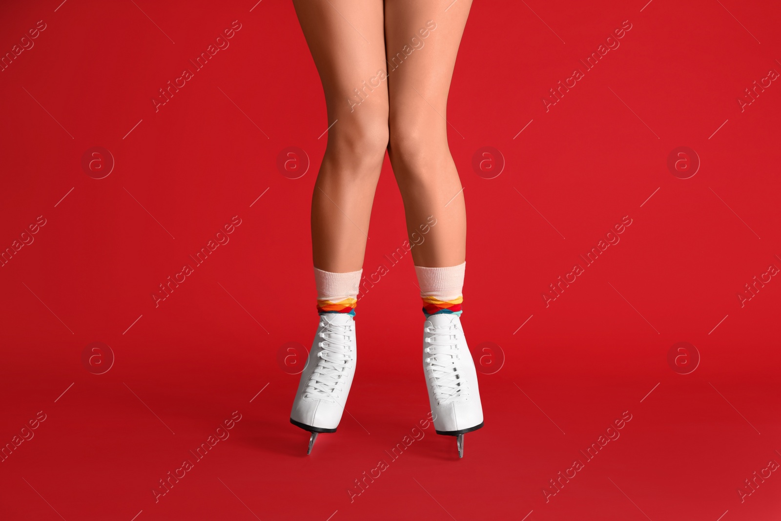 Photo of Woman in elegant white ice skates on red background, closeup of legs