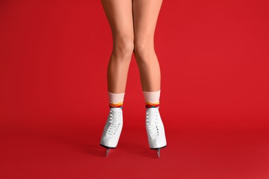 Photo of Woman in elegant white ice skates on red background, closeup of legs
