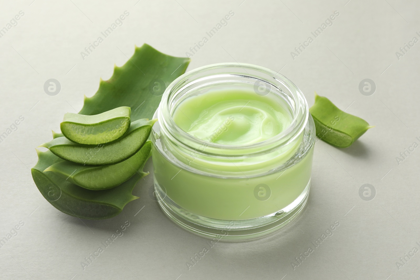 Photo of Jar with cream and cut aloe leaf on light grey background, closeup