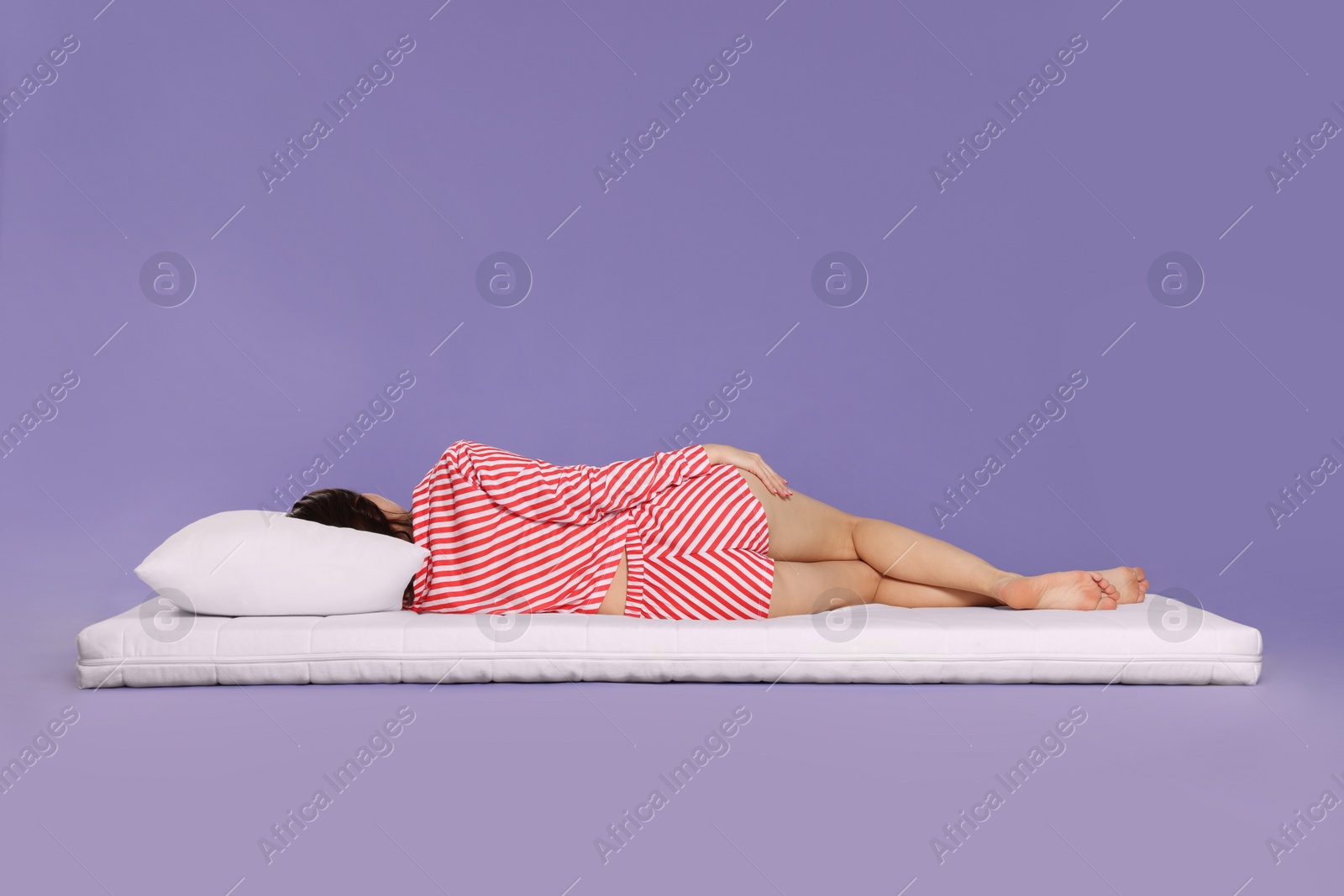 Photo of Young woman sleeping on soft mattress against light purple background, back view