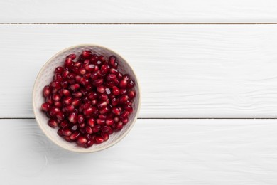 Photo of Ripe juicy pomegranate grains in bowl on white wooden table, top view. Space for text