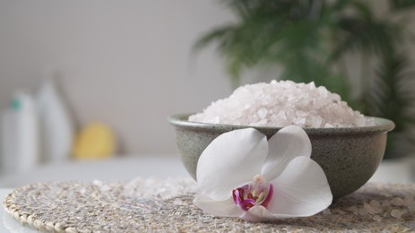 Photo of Bowl with bath salt and flower on wicker mat indoors, space for text