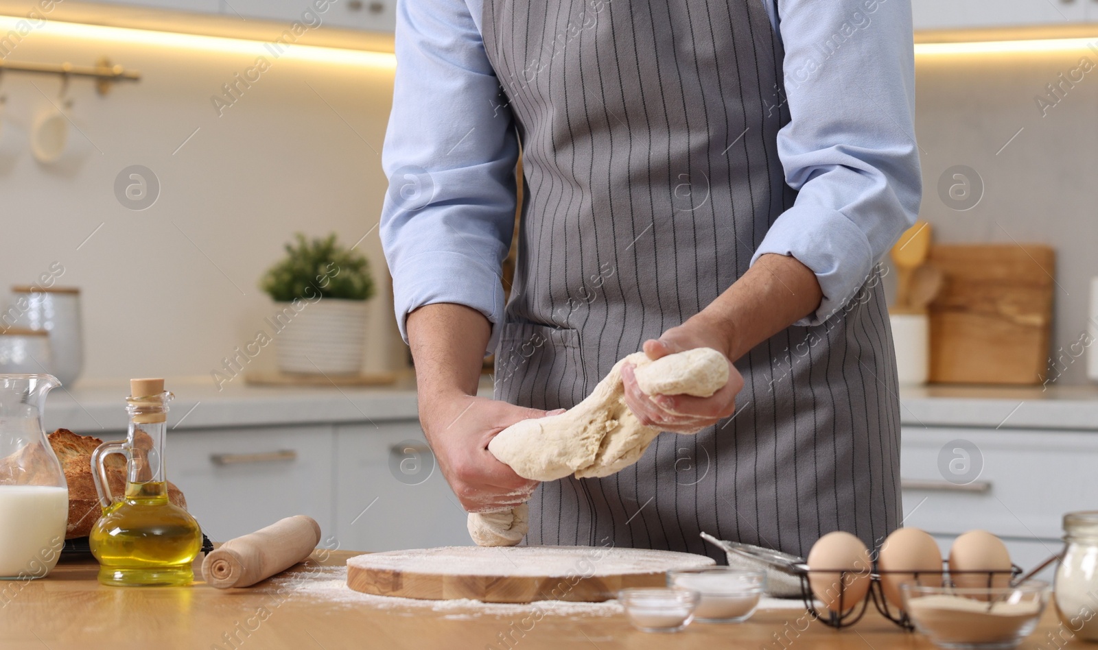 Photo of Making bread. Man kneading dough at wooden table in kitchen, closeup