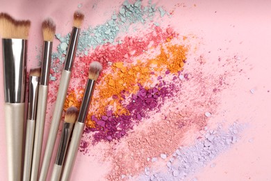 Photo of Makeup brushes and scattered eye shadows on pink background, flat lay