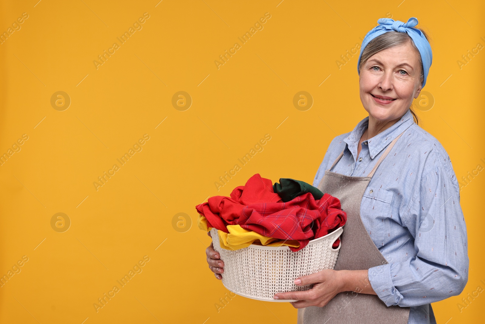 Photo of Happy housewife with basket full of laundry on orange background, space for text