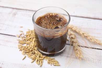 Photo of Cup of barley coffee, grains and spikes on wooden table, closeup