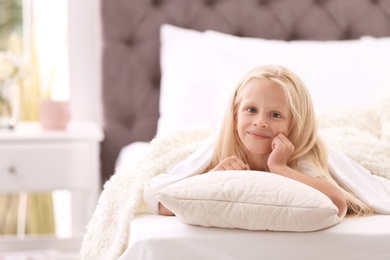 Cute little girl with pillow lying in bed at home