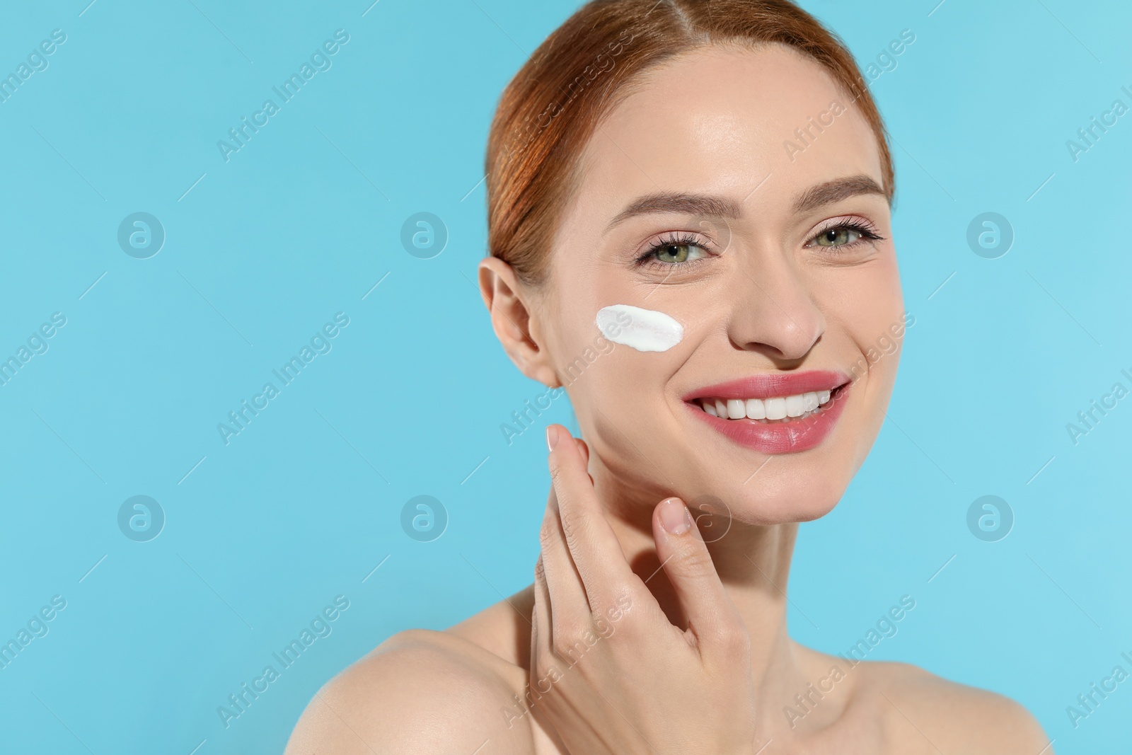 Photo of Beautiful young woman with sun protection cream on her face against light blue background, space for text