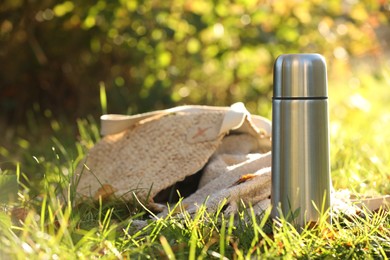 Photo of Metal thermos and bag with blanket on green grass outdoors