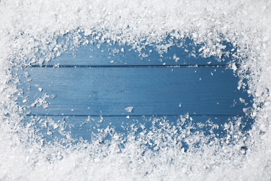 Photo of Frame of white snow on blue wooden background, top view with space for text. Christmas season