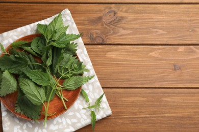 Photo of Fresh stinging nettle leaves on wooden table, top view. Space for text