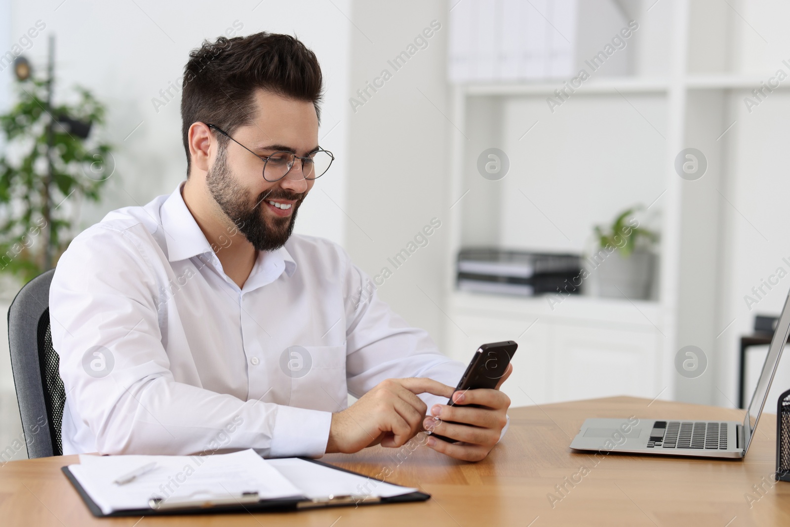 Photo of Handsome young man using smartphone at wooden table in office