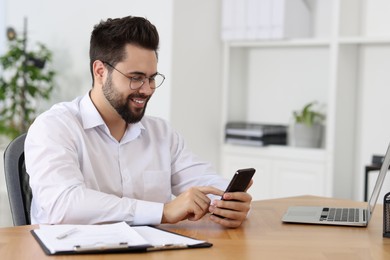 Handsome young man using smartphone at wooden table in office