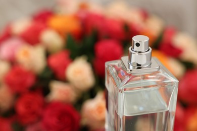 Bottle of perfume against bouquet of beautiful roses, closeup. Space for text