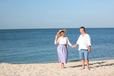 Happy mature couple holding hands at beach on sunny day