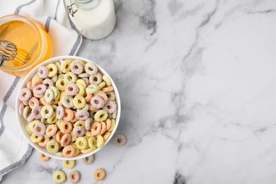 Photo of Tasty cereal rings in bowl, milk and honey on white marble table, flat lay. Space for text