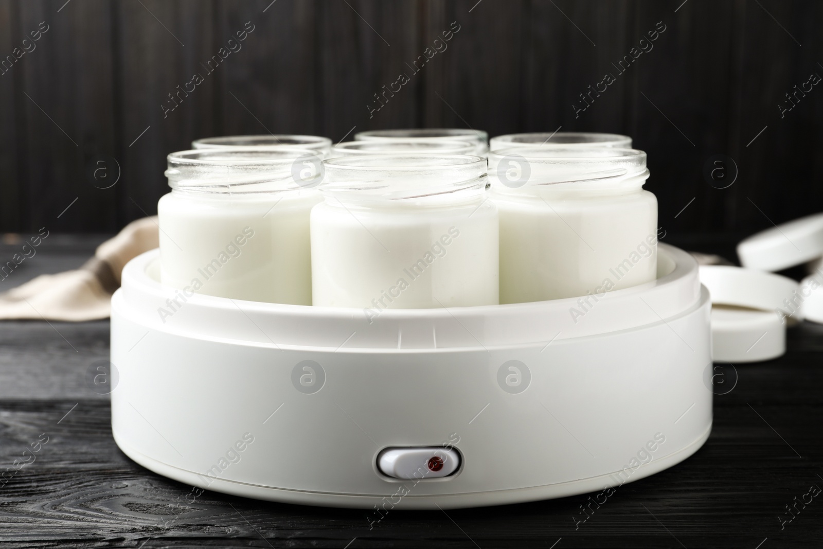 Photo of Modern yogurt maker with full jars on black wooden table