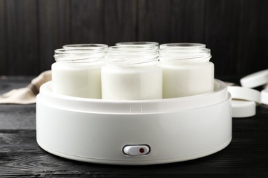 Modern yogurt maker with full jars on black wooden table