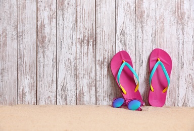 Bright flip flops and sunglasses on sand near wooden wall, space for text. Summer beach accessories