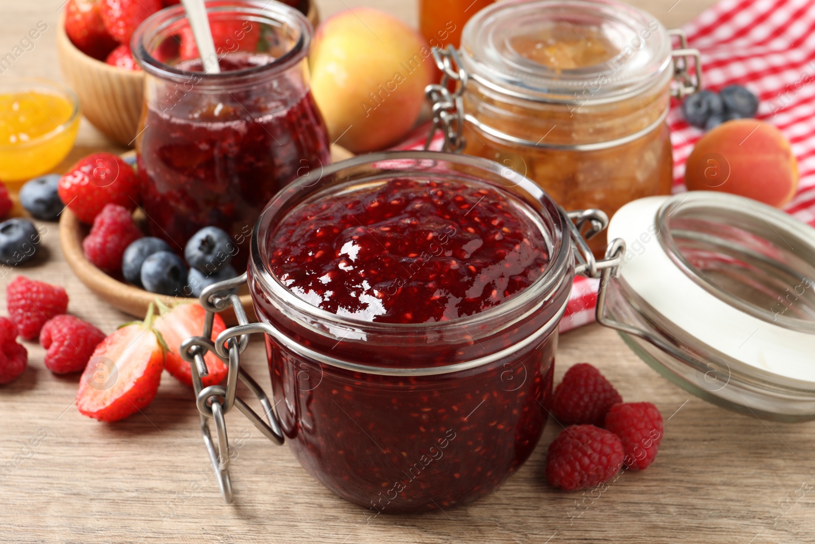 Photo of Jars with different jams and fresh fruits on wooden table, closeup