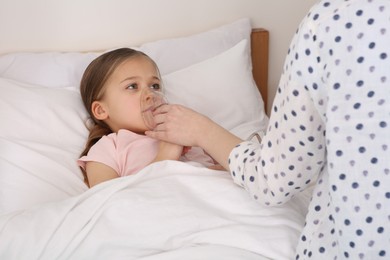 Mother helping her sick daughter with nebulizer inhalation in bedroom